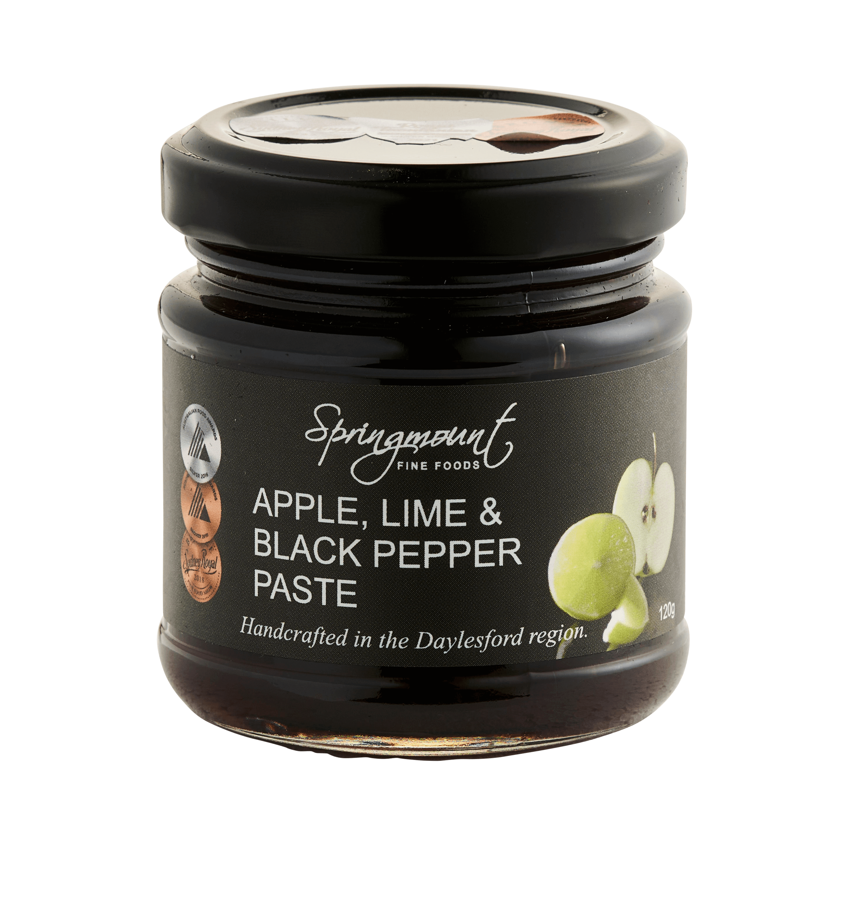 A jar of Springmount Apple, Lime & Black Pepper Paste sits on a light grey background. It has a black lid and a dark grey label with award stickers. The label shows an illustration of a lime and sliced apple. The paste is a deep reddish-brown colour.