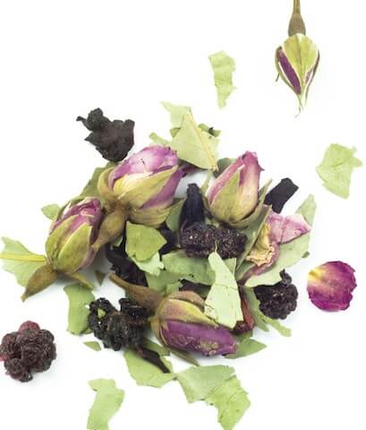 A scattering of dried rosebuds, green leaves, and dark berries, shot from above on a white background. The ingredients are textured and colourful, with a focus on the pink and purple hues.