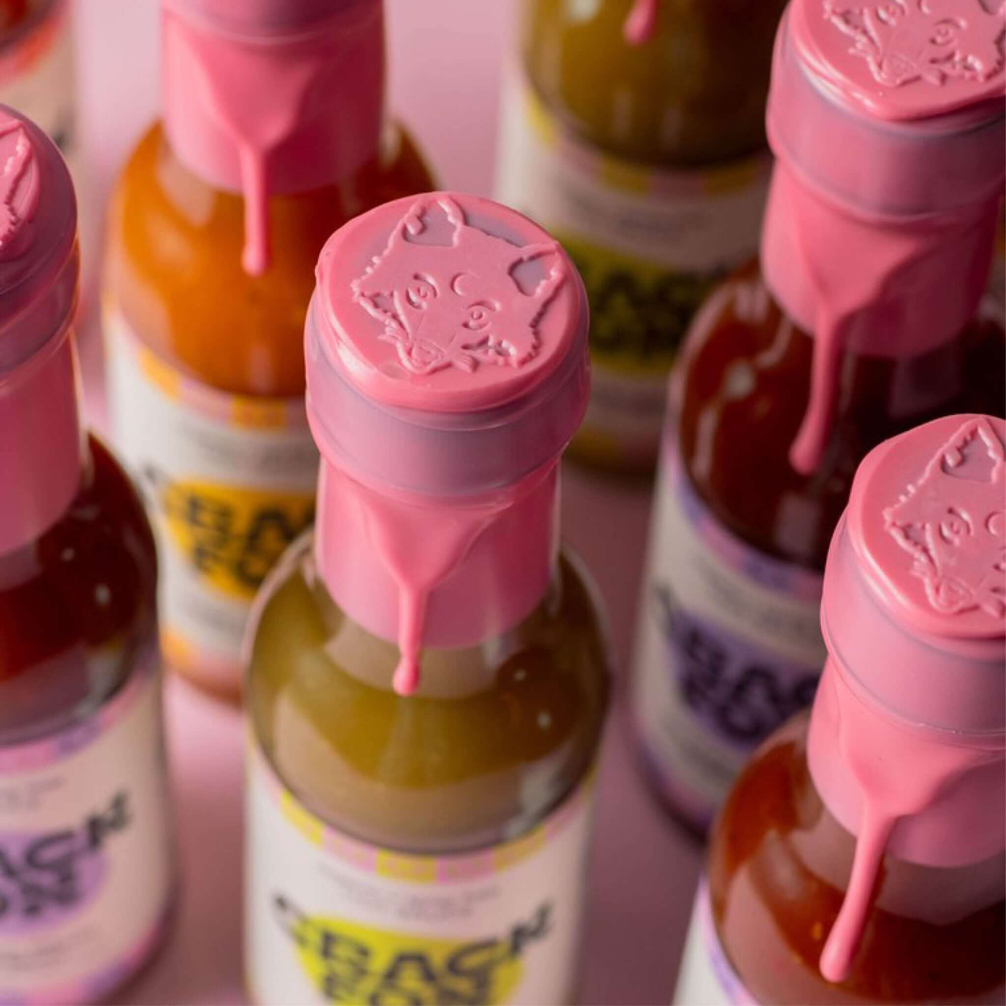 Several bottles of sauce with pink wax seals featuring an embossed fox face design. The wax drips down the necks, and the labels, though not fully legible, add a unique artistic touch.