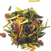 A colourful mix of loose green tea, dried fruit pieces (red & dark), herbs, and yellow strips, scattered on a white background. Shot from above, showing texture and variety.