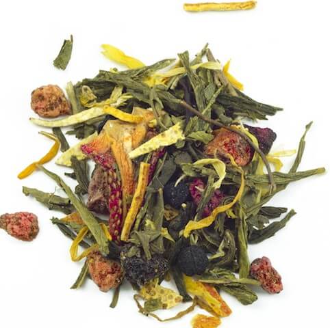 A colourful mix of loose green tea, dried fruit pieces (red & dark), herbs, and yellow strips, scattered on a white background. Shot from above, showing texture and variety.