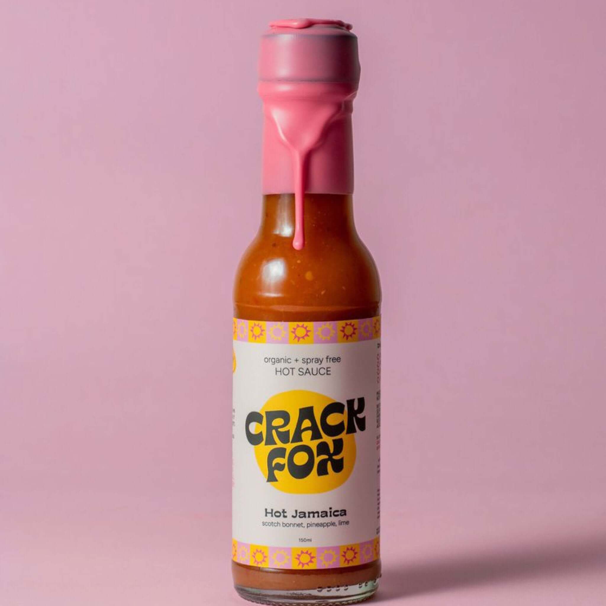 A 150 ml bottle of Crack Fox hot sauce with a pink wax seal on a pink background. Label reads &quot;organic + spray free HOT SAUCE,&quot; &quot;Hot Jamaica,&quot; and lists the ingredients.