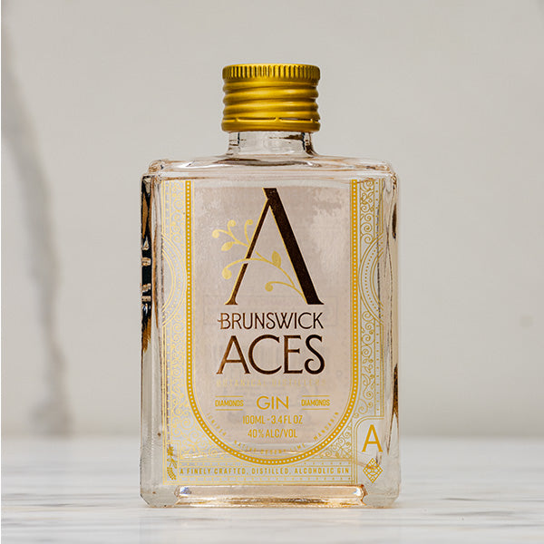 A square bottle of Brunswick Aces Gin with a gold cap. The label features a stylized "A" and ornate details, indicating it's a craft gin with a 40% alcohol content. The bottle is small, likely a miniature.