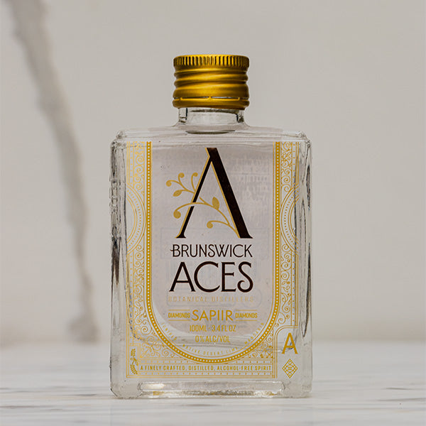 A miniature square bottle of Brunswick Aces Sapiir, an alcohol-free distilled botanical spirit. The label features an ornate "A" logo and highlights the use of native Australian desert lime and mango.