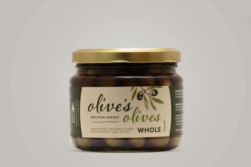 A jar of "Olive's Olives" from Macedon Ranges. Hand-picked, naturally cured, whole olives are visible through the glass. Gold lid on a grey background.
