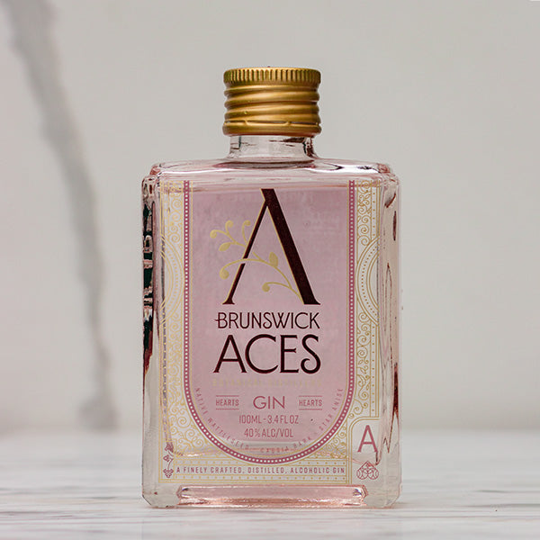 A miniature square bottle of Brunswick Aces Hearts Gin with a gold cap. The label features an ornate "A" logo and highlights the use of premium botanicals. The gin is 100ml with an alcohol content of 40%.