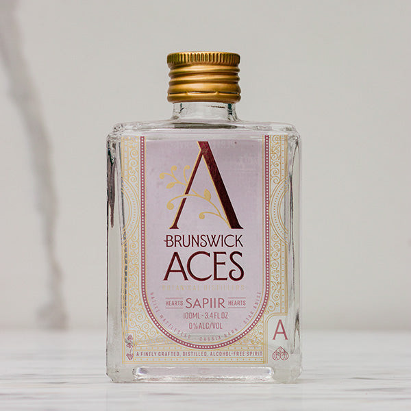 A miniature square bottle of Brunswick Aces Sapiir, an alcohol-free distilled botanical spirit. The label features an ornate "A" logo and highlights the use of native Australian desert lime and mango. The bottle is 100ml and 0% alcohol.