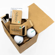 Open box containing white "tomorrow" golf balls, "naiteev" boxes with black and white golf tees, black and white markers, and a card thanking for making a difference.