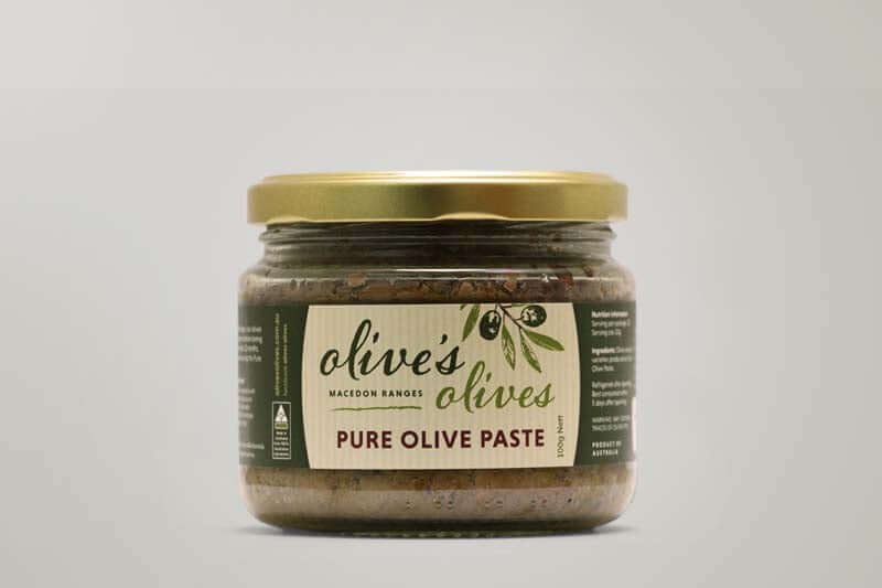 A glass jar of "Olive's Olives" Pure Olive Paste from the Macedon Ranges. The jar has a golden lid and is filled with a dark green olive paste. The label features a hand-drawn illustration of olives and the words "Pure Olive Paste" in a handwritten style.
