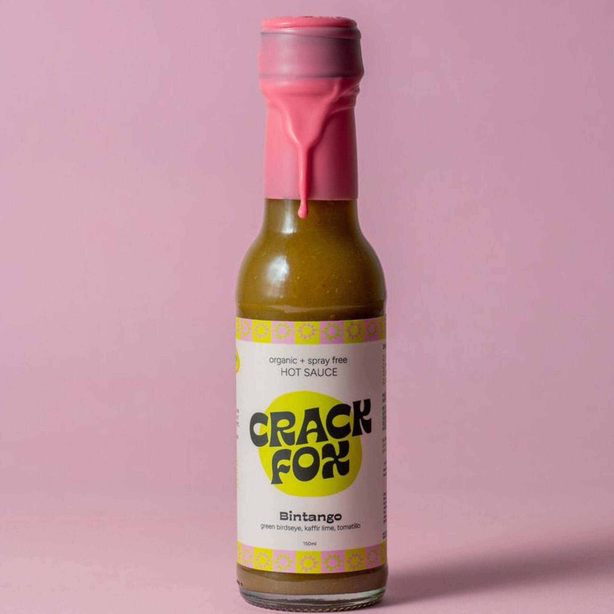 A 150ml bottle of Crack Fox hot sauce with a pink wax seal. Label reads "organic + spray free HOT SAUCE," "Bintango," and lists ingredients: "green birdseye, kaffir lime, tomatillo."