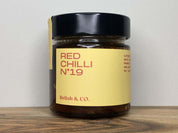 Close-up of Relish & Co. Red Chilli relish jar. Yellow label, black lid, red contents visible.