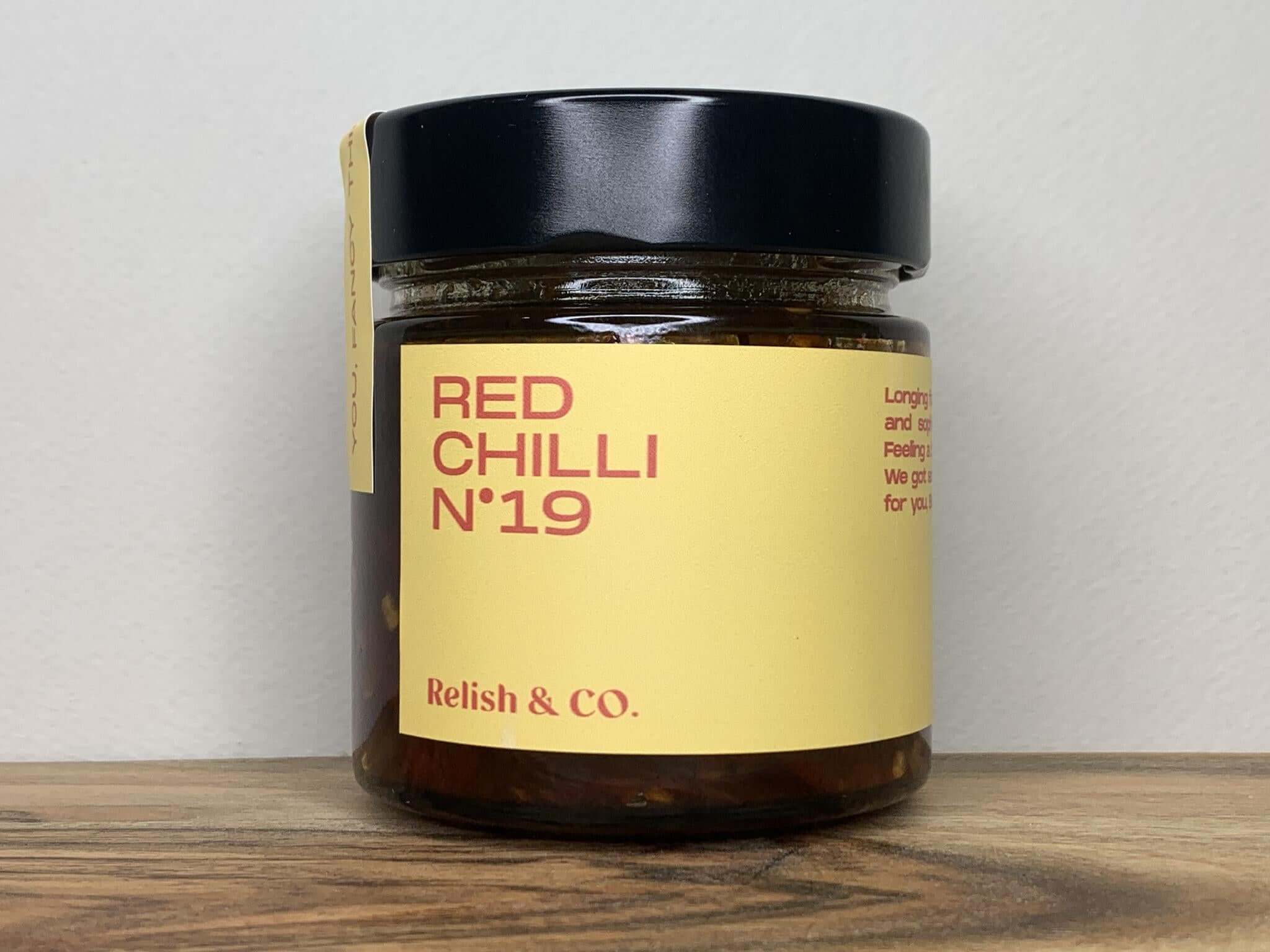 Close-up of Relish & Co. Red Chilli relish jar. Yellow label, black lid, red contents visible.