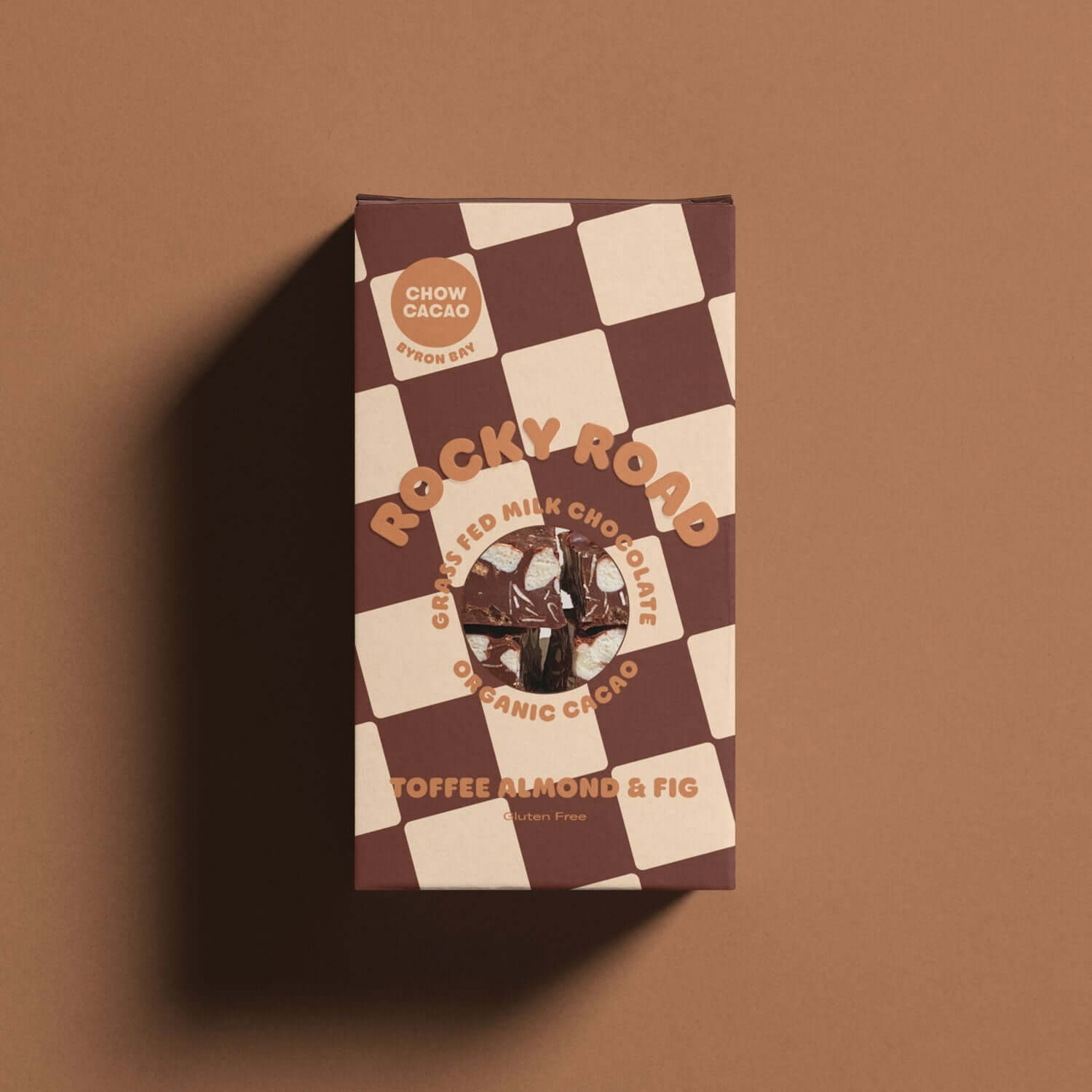 A top-down view of a rectangular box of chocolate. The box is brown with a checkered pattern and the words "Rocky Road" and "Toffee, Almond & Fig" written on it. The brand name "Chow Cacao" is also visible.