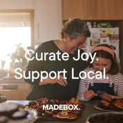 Two people, one adult and one child, are in a kitchen preparing food. They have trays of dried fruits and other items on the counter. The text on the image reads "Curate Joy Support Local" and "MADEBOX."