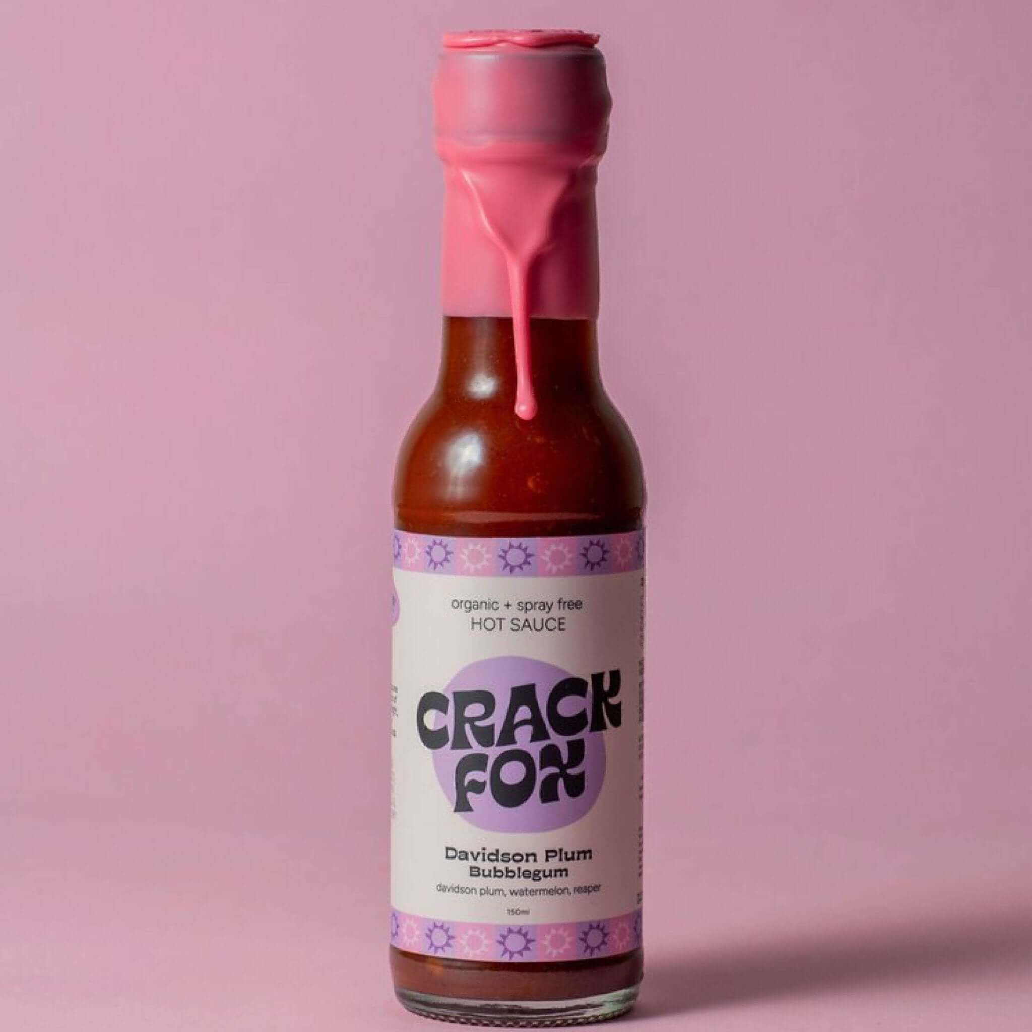 A 150ml bottle of Crack Fox hot sauce with a pink wax seal on a solid pink background. The label reads &quot;Davidson Plum Bubblegum&quot; and lists ingredients: &quot;davidson plum, watermelon, reaper.&quot;