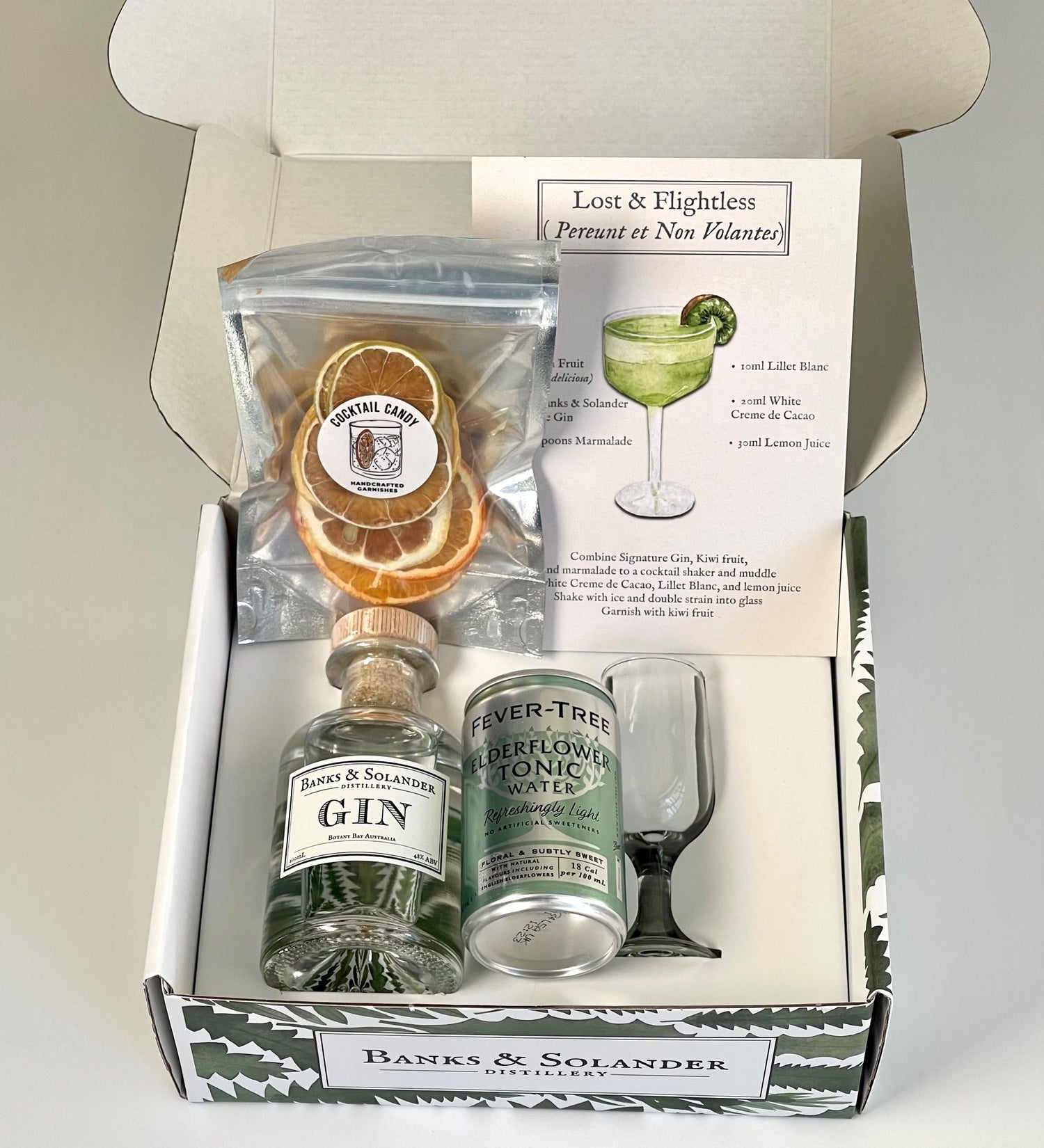 A gift box containing all the ingredients to make a "Lost & Flightless" cocktail. Inside are a miniature bottle of Banks & Solander Signature Gin, a can of Fever-Tree Elderflower Tonic, dehydrated citrus slices, a small glass, and a recipe card.